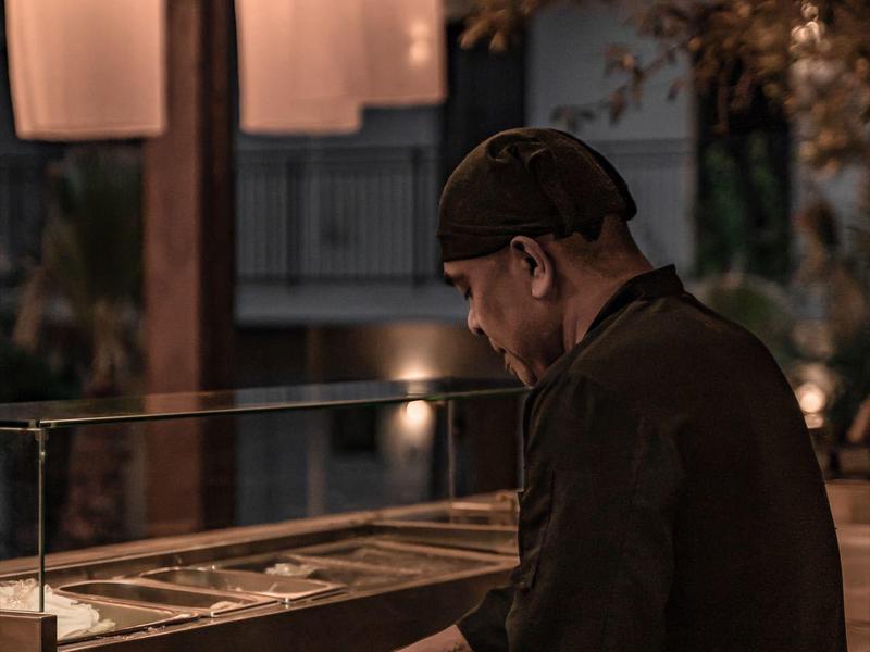 Cuoco con abiti scuri che lavora in una cucina all'aperto elegante di notte.