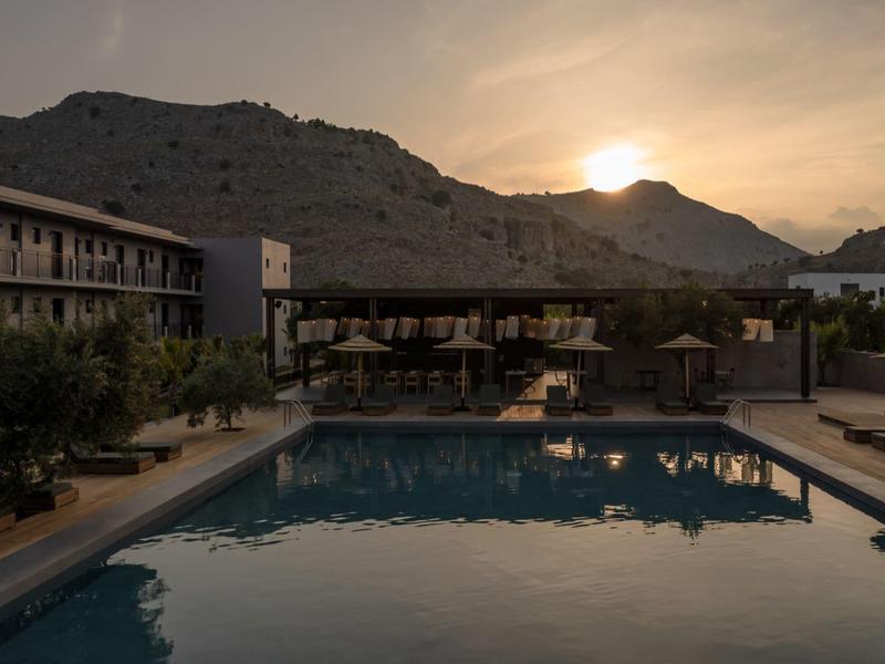 Una piscina tranquilla al tramonto con edifici e colline sullo sfondo.