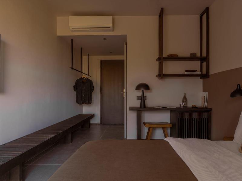 Camera d'albergo semplice con letto, sgabello di legno, appendiabiti e aria condizionata