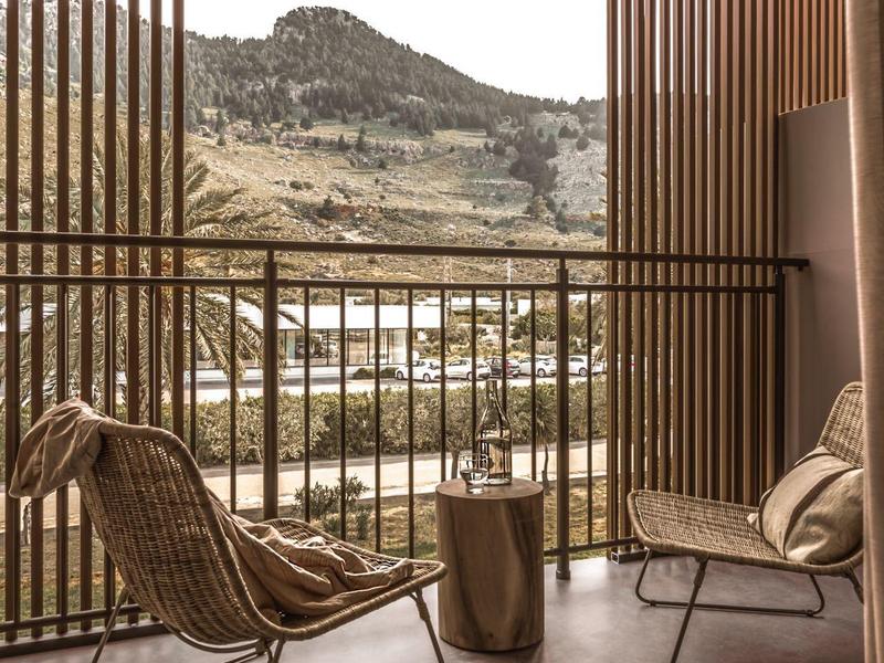 Balcone con due sedie e vista sulla montagna dietro stecche di legno verticali.