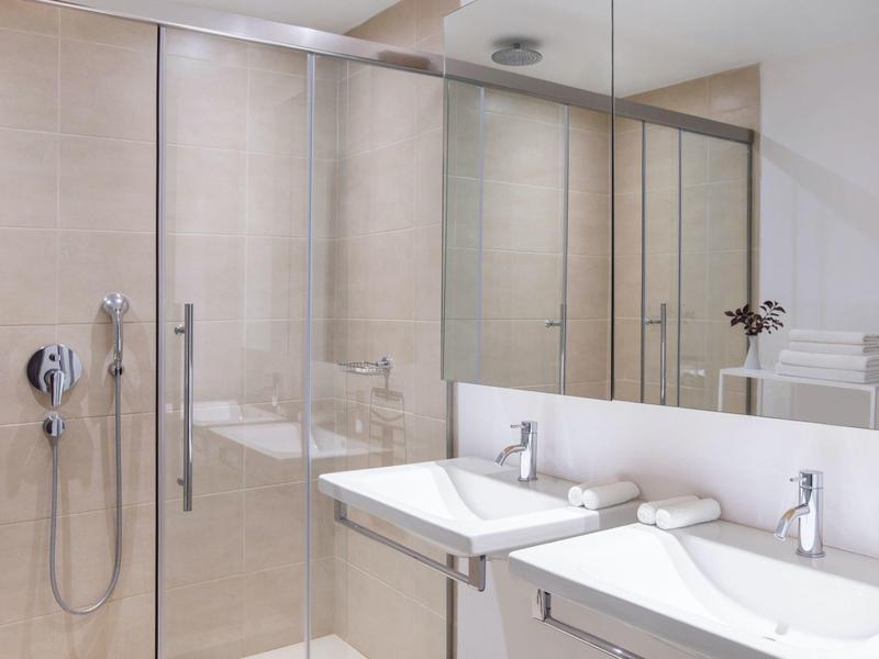 Bagno moderno con lavandini bianchi, asciugamani e grande parete specchio