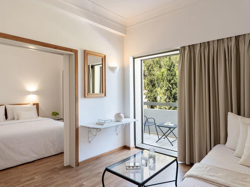 Camera d'hotel luminosa con letto, divano, piccolo terrazzo e vista sul verde.