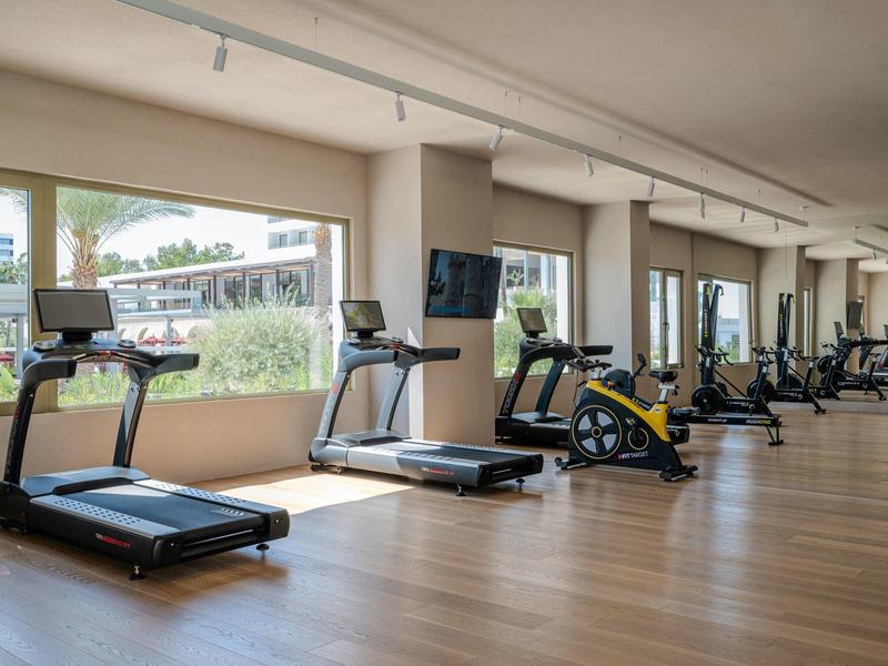 Attrezzature fitness moderne in una stanza luminosa con grandi finestre e pavimento in legno.