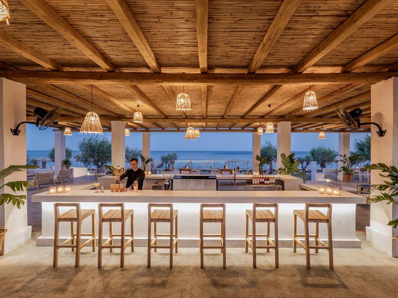 Area bar moderna con sgabelli in legno e vista mare in una lounge aperta.