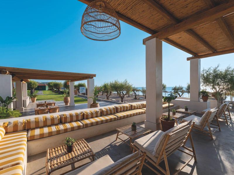 Terrazza dell'hotel con posti a sedere, vista sul giardino e sul mare sotto un cielo sereno.