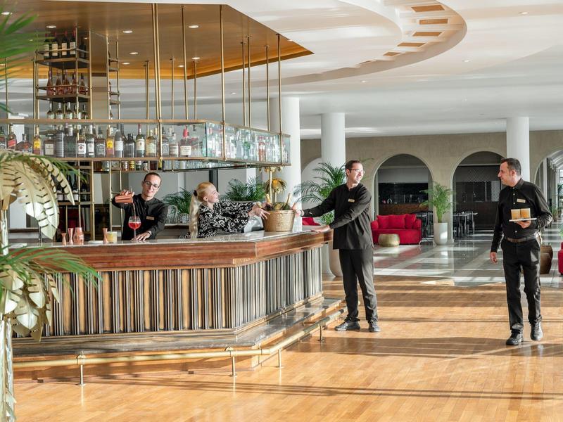 Bar dell'hotel con baristi, grandi finestre e pavimento in legno chiaro in un ambiente moderno.