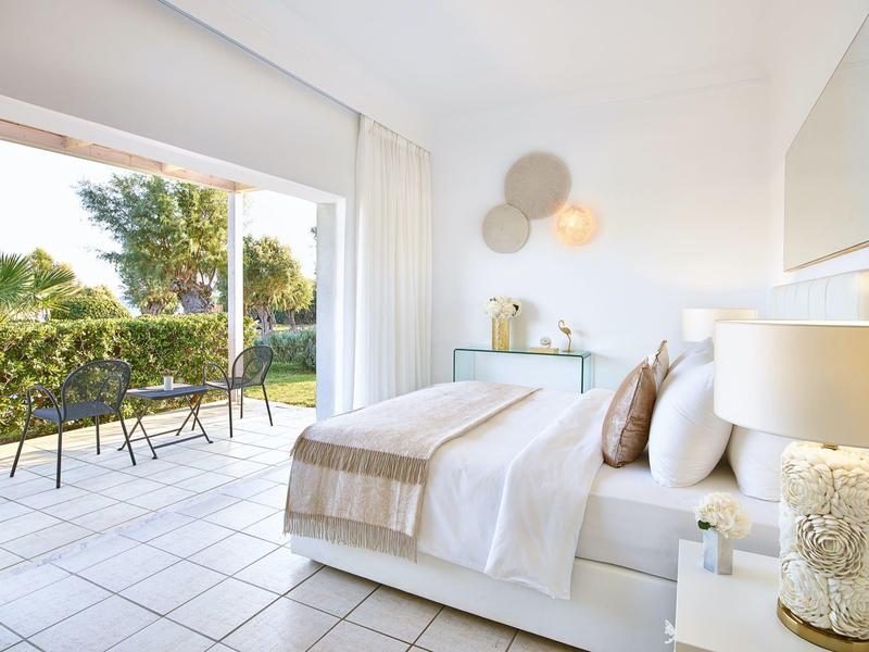 Camera d'hotel luminosa con letto matrimoniale, cuscini comodi e terrazza con vista sul giardino.