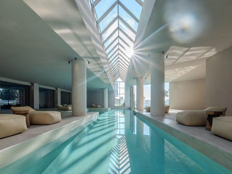 Piscina interna in hotel moderno con luce naturale dal tetto in vetro e aree salotto.