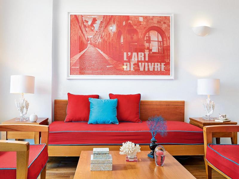 Soggiorno moderno con divano rosso, cuscini colorati e opera d'arte sulla parete.