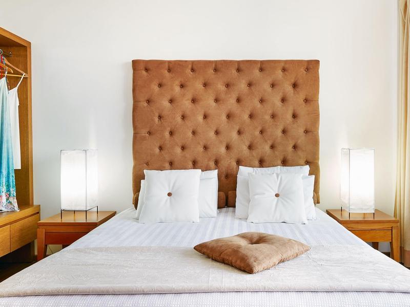 Camera d'hotel moderna con letto grande, testiera imbottita e due comodini con lampade.