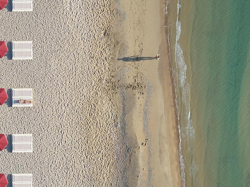 Spiaggia sabbiosa vuota con file di ombrelloni e sedie accanto al mare calmo.