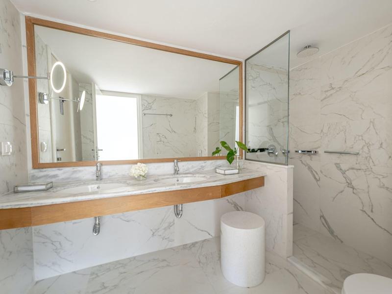 Bagno moderno con grande specchio, doppi lavabi e marmo bianco.