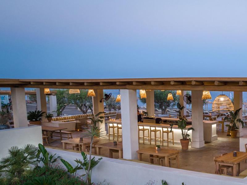 Area bar aperta in hotel con sedie e tavoli in legno, circondata dalla natura al tramonto.