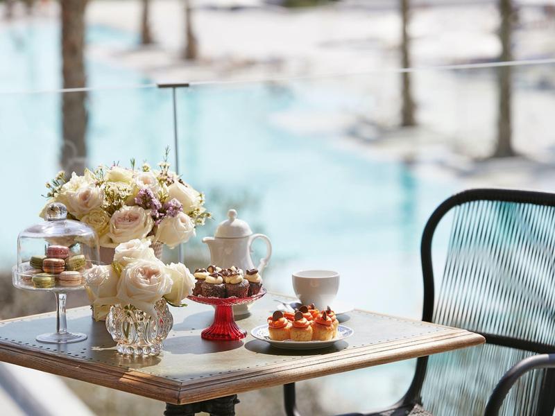 Un tavolo vicino alla piscina con dolci, fiori e servizio da tè alla luce del giorno.