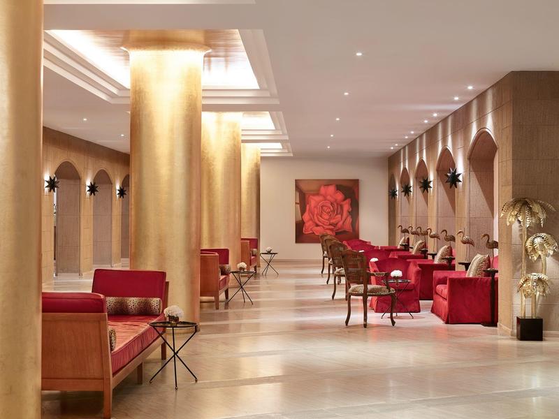 Elegante area lounge dell'hotel con divani rossi, colonne dorate e illuminazione decorativa.