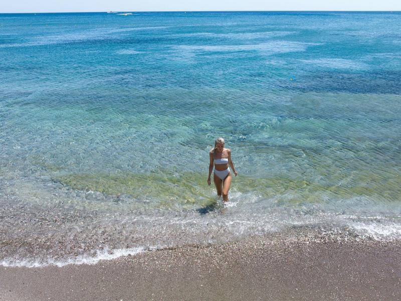 Donna in bikini in piedi nell'acqua turchese trasparente sulla spiaggia sabbiosa.