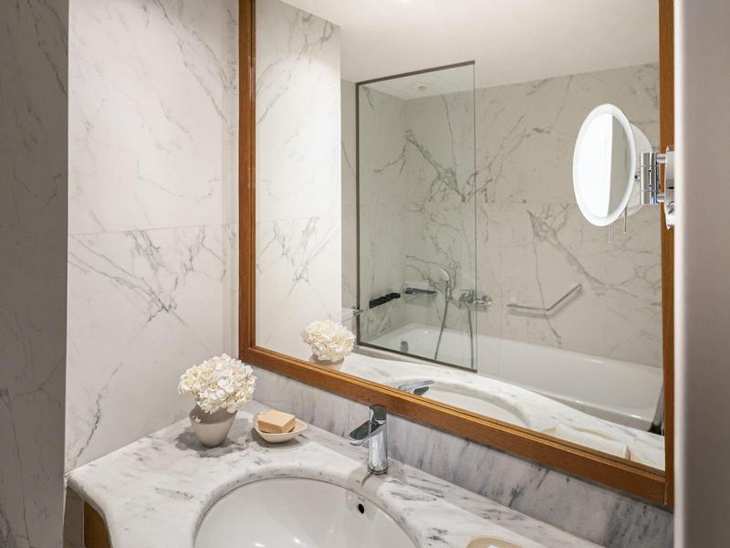 Area bagno moderna con lavandino, grande specchio e vasca da bagno con parete in vetro.