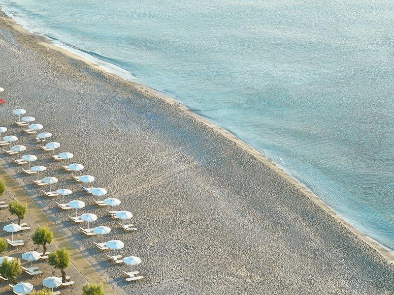 Spiaggia con file di ombrelloni bianchi e lettini accanto a un'acqua calma.