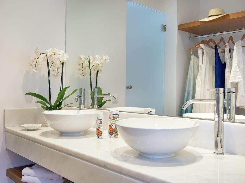 Bagno moderno con due lavandini bianchi, orchidee e accappatoi appesi.