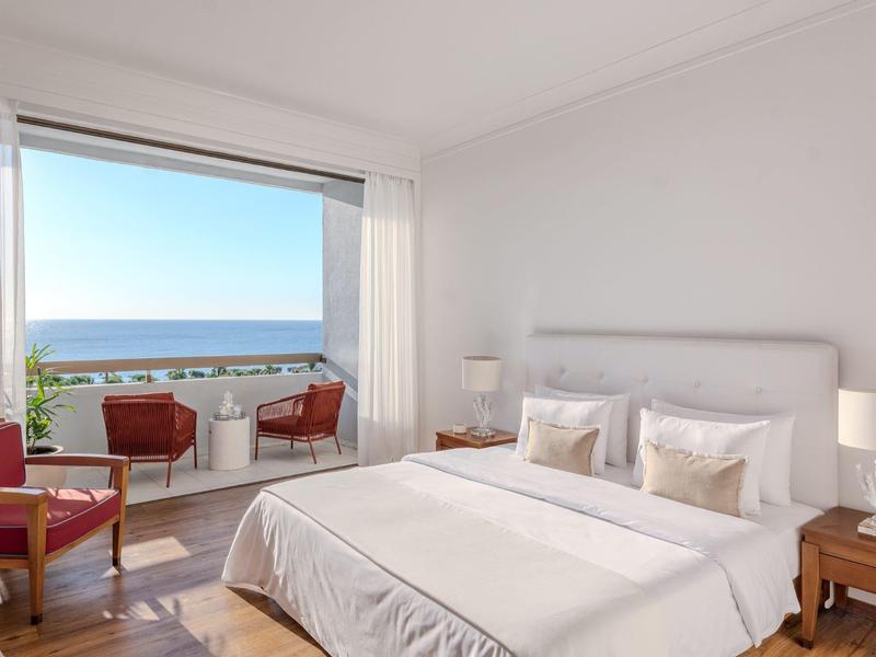 Camera d'albergo luminosa con letto matrimoniale e balcone con vista sul mare con sedie.