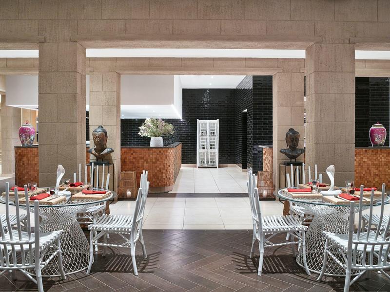 Zona pranzo dell'hotel moderna con tavoli rotondi, sedie in filo metallico e decorazioni eleganti.