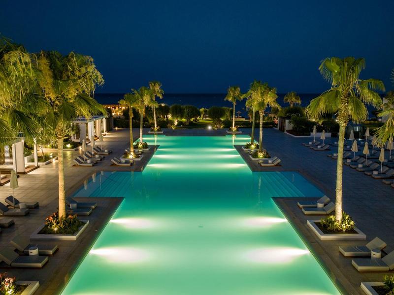 Piscina illuminata con lettini e palme di notte in un resort.
