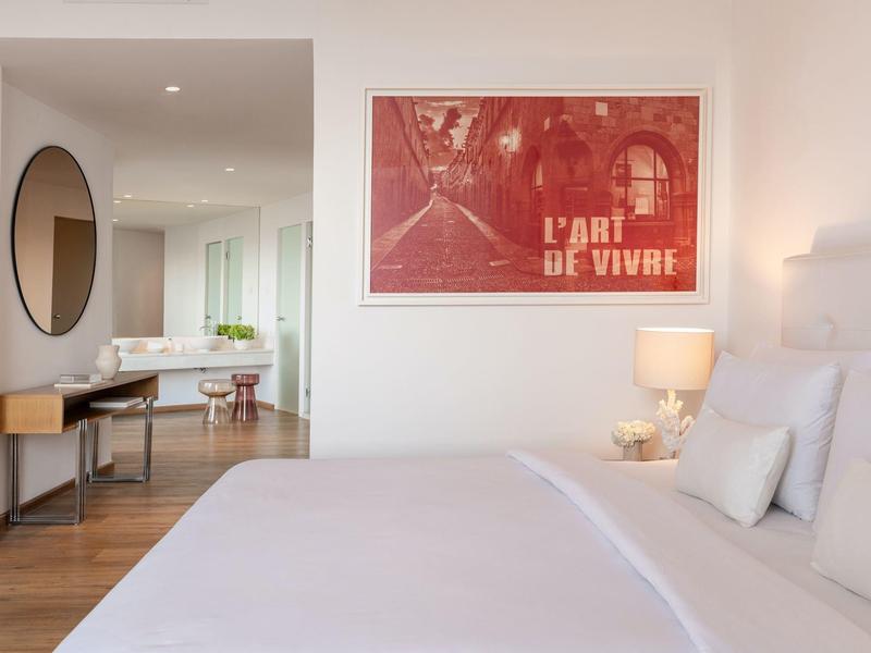 Camera d'hotel moderna con letto grande, arte murale rossa e scrivania con specchio rotondo.