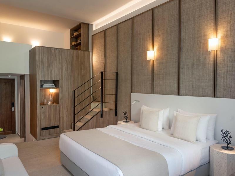 Camera d'hotel moderna con grande letto, unità di stoccaggio e scala per soppalco.