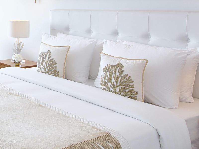 Camera luminosa con biancheria bianca e cuscini decorativi con motivi vegetali.