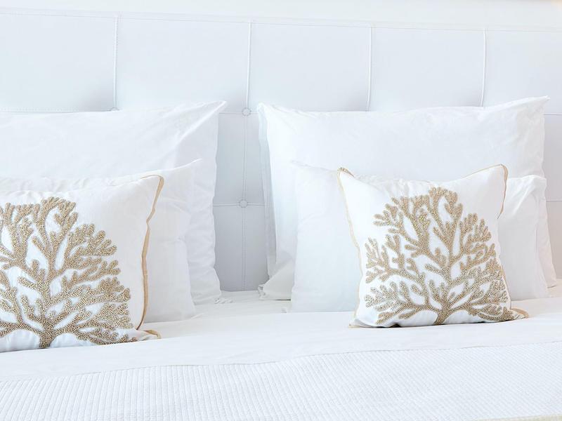 Letto bianco con due piccoli cuscini a tema corallo in una stanza luminosa.