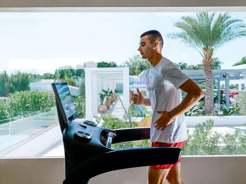 Uomo che si allena su un tapis roulant su una terrazza d'hotel con vista su palme e mare.