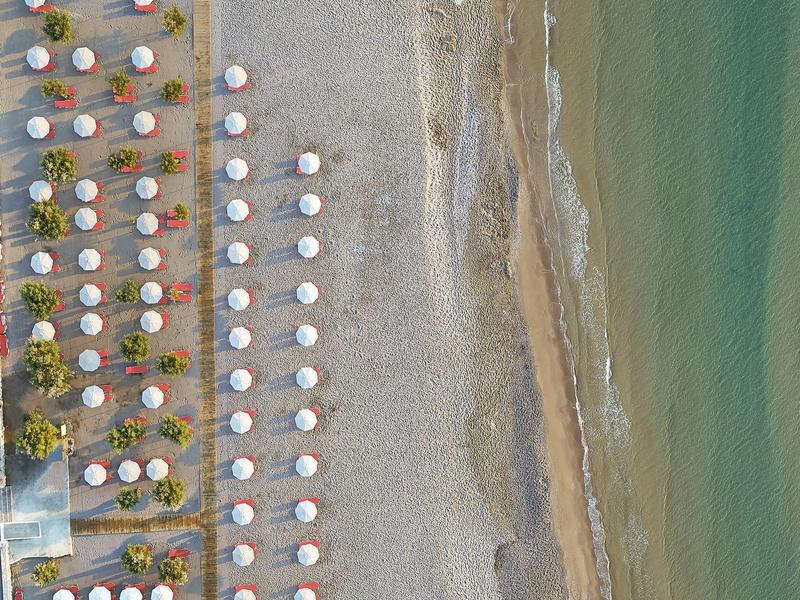 Veduta aerea di una spiaggia con file di ombrelloni bianchi e mare blu.