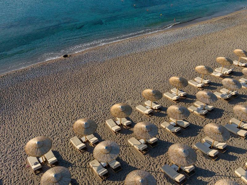 Lettini vuoti con ombrelloni rotondi sulla riva sabbiosa e mare calmo sullo sfondo.