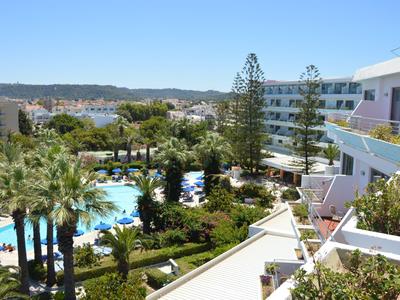 Hotelanlage mit mehreren Pools, Palmen und Ausblick auf eine Stadt und das Meer bei klarem Himmel.
