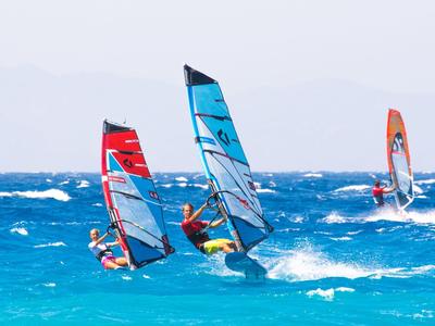 Drei Windsurfer gleiten auf blauem Meer bei leicht bewölktem Himmel.