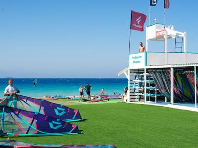 Windsurfer am Strand mit grünem Rasen und klarem blauen Himmel am Meer.
