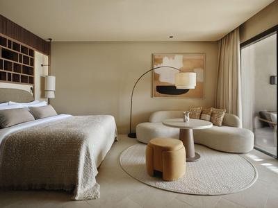 Chambre d'hôtel confortable avec lit double, canapé, tapis rond et accès au balcon.