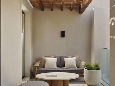 Espace assise moderne avec plafond en bois, canapé gris, deux coussins, table ronde et plante en pot.