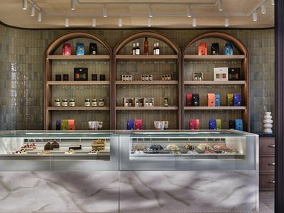 Bar d'hôtel moderne avec étagères en bois, spiritueux, verres et comptoir éclairé avec desserts.