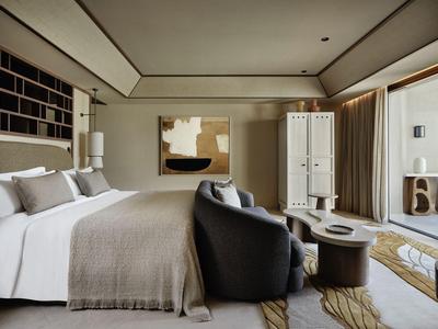 Chambre d'hôtel moderne avec grand lit, fauteuils confortables et accès à un balcon avec vue.