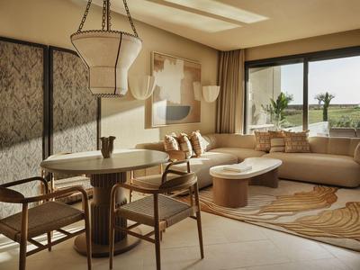 Salon lumineux avec une table à manger moderne, des chaises et un canapé d'angle beige près d'une grande fenêtre.