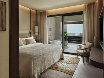 Chambre lumineuse avec grand lit et accès à un balcon avec vue sur la mer.