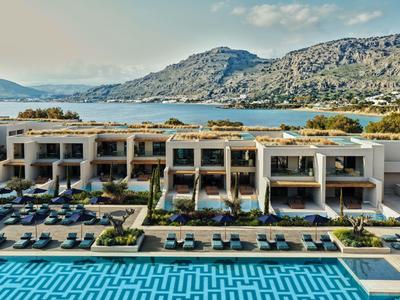 Complexe hôtelier moderne avec piscine, transats et vue sur la mer et les collines.
