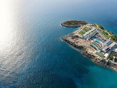 Vue aérienne d'une petite île rocheuse avec des installations hôtelières au bord de la mer bleue claire.