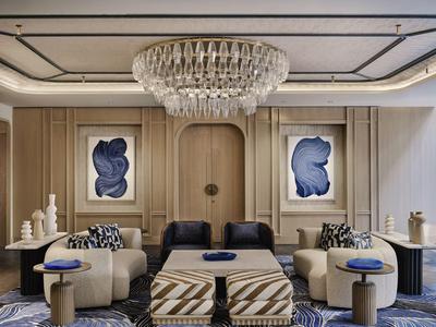 Espace lounge d'hôtel élégant avec fauteuils confortables, pouf à motifs et grand lustre en cristal.