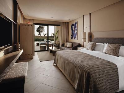 Chambre d'hôtel moderne avec grand lit, coin salon et balcon avec vue sur la nature.