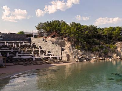 Hôtel moderne avec terrasse au bord de la mer et rochers, entouré d'arbres et d'eau claire.