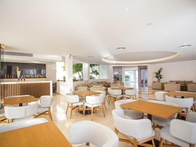 Área de lobby de hotel luminosa con muebles modernos de madera y sillones blancos en ambiente cálido.