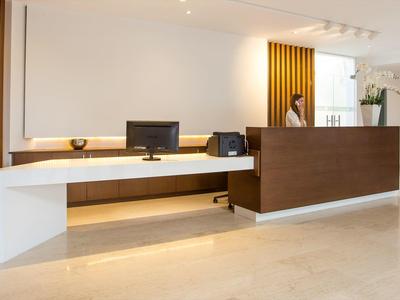 Recepción moderna de hotel con mostrador de madera, computadora y diseño minimalista y claro.