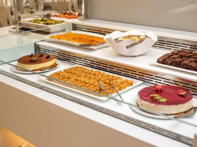 Vitrina con diferentes platos de postres en un buffet de hotel con ambiente luminoso.